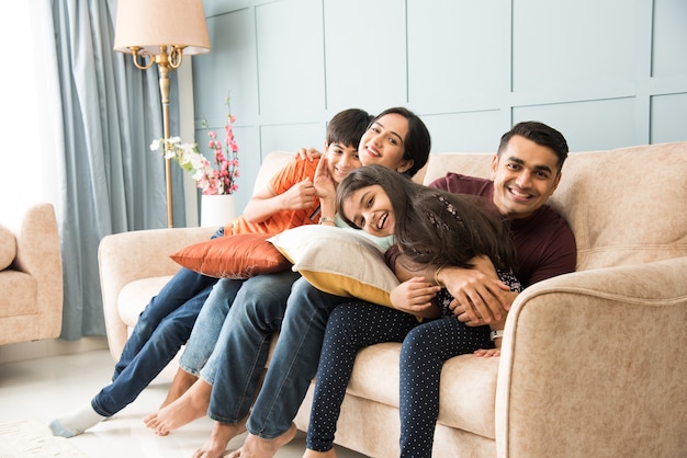 Portrait of happy Indian Asian young family while sitting on sofa, lying on floor or sitting against wall