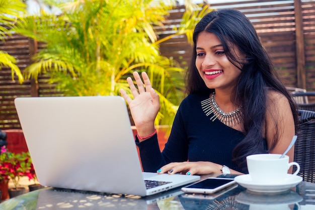 Portrait of a happy Indian business woman working on laptop at summer cafe.remote work freelance serfing