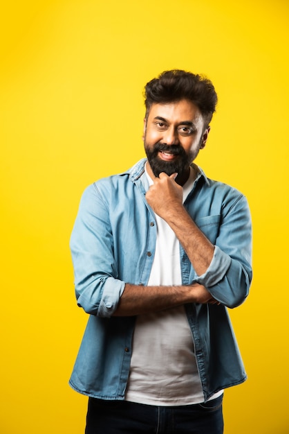 Portrait of Happy Indian young bearded man with arms crossed on yellow