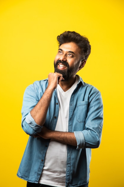 Portrait of Happy Indian young bearded man with arms crossed on yellow