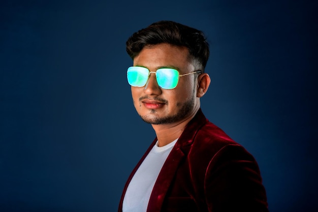 Portrait of Happy Indian young man wearing a blazer with eyeglasses posing on a blue background