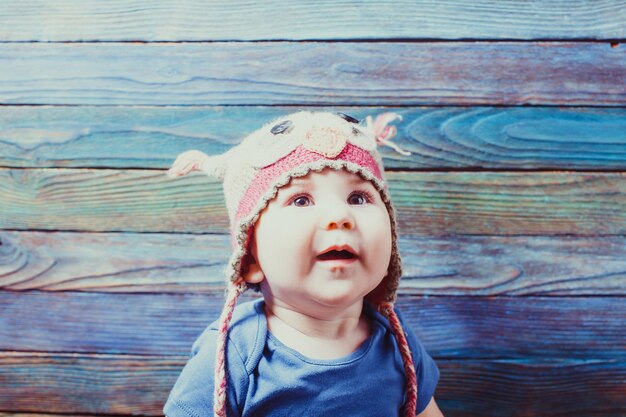 Portrait of happy infant baby in owl hat over wooden background