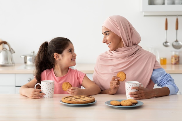 幸せなイスラムの家族のママと娘がキッチンでスナックを食べるの肖像画