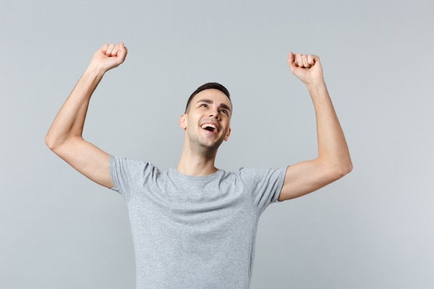 Portrait of happy joyful young man in casual clothes looking up, rising hands, clenching fists like winner 