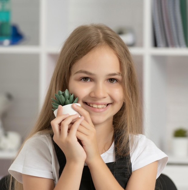 幸せな子供の肖像画は、学校の教室で鉢植えの植物を保持します