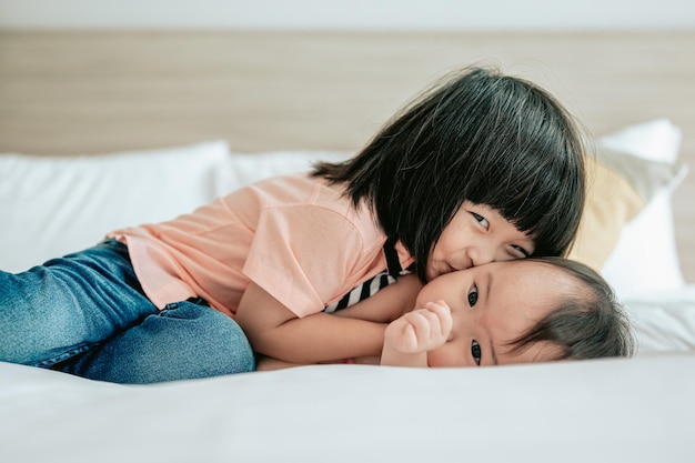 Portrait of happy kids playing in white bedroom Little boy and girl brother kissing and hugging little sister on the bedHappy family lifestyle concept