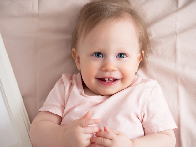 Portrait of a happy laughing baby, with a funny expression on his face. A small beautiful girl with blue eyes smiles cheerfully, the first teeth are visible.