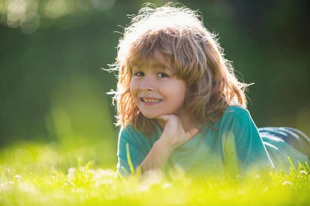 Portrait of a happy laughing child laying on grass in summer nature park close up positive kids face