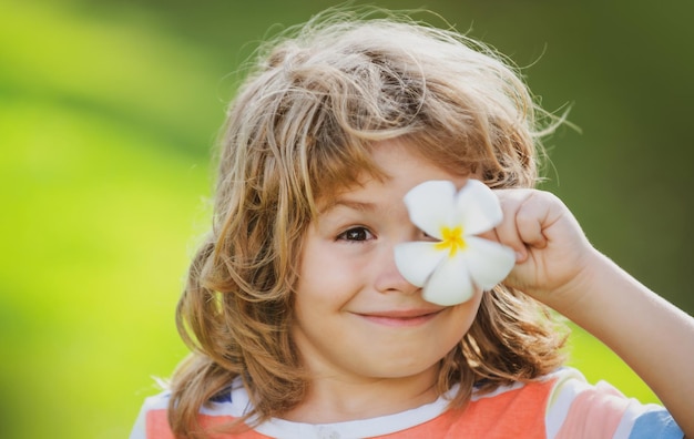 プルメリアの花のクローズアップポジティブな子供の顔が目を覆っている幸せな笑いの子供の肖像画