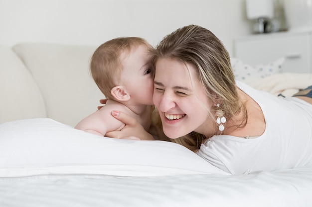 Portrait of happy laughing mother playing with her baby boy on bed