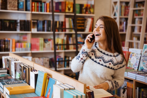 Portrait of a happy laughing woman talking on mobile phone while sitting in library