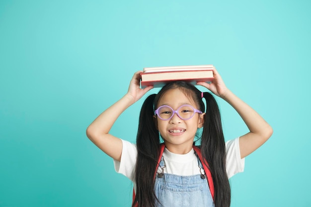 Ritratto di bambina pigra felice che copre la testa con il libro e sorride alla macchina fotografica