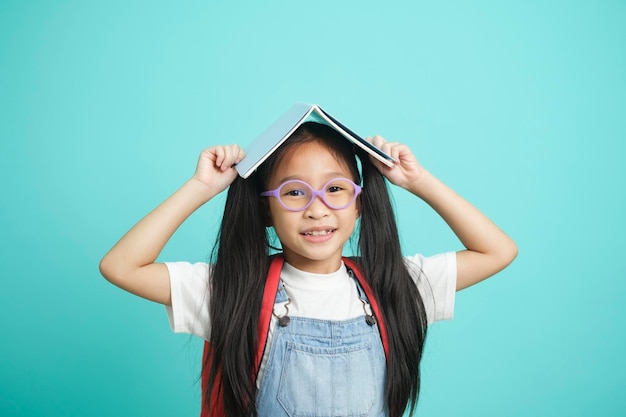 Ritratto di bambina pigra felice che copre la testa con il libro e sorride alla macchina fotografica