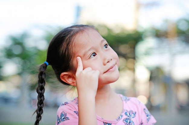 Portrait of happy little Asian child in garden with thinking and looking up.