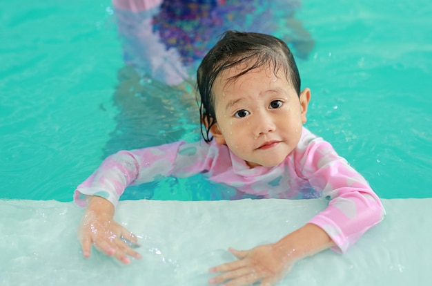 Photo portrait of happy little asian child girl learning to swim in pool.