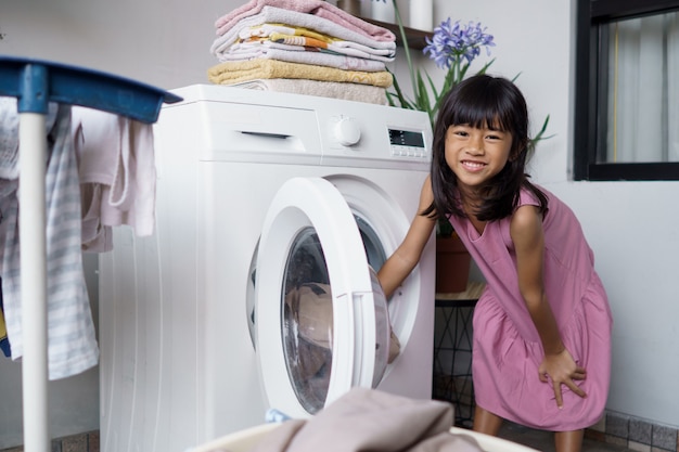 Portrait of happy little asian girl doing laundry at home