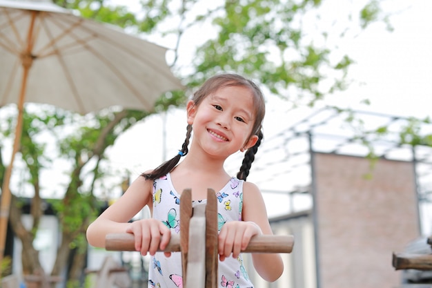 屋外の庭で木のおもちゃの馬を遊んで幸せの小さなアジアの女の子の肖像画。