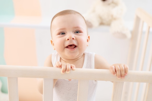 Portrait of a happy little baby girl or boy in a white bodice on the bed in the bedroom a baby with blue eyes