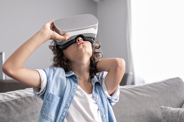 Portrait of happy little boy child using virtual reality headset vr glasses gesturing at home fun