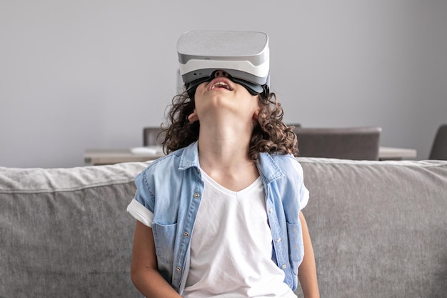 Portrait of happy little boy child using virtual reality headset vr glasses gesturing at home fun