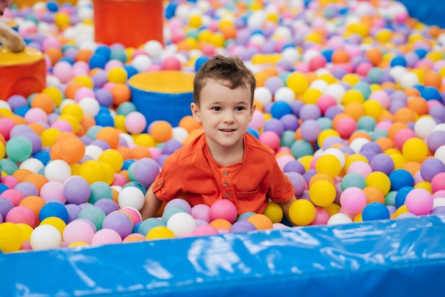 Portrait of a happy little boy jumping merrily into a dry pool with colorful balloons A toddler boy is playing and having a good time at the children's entertainment center