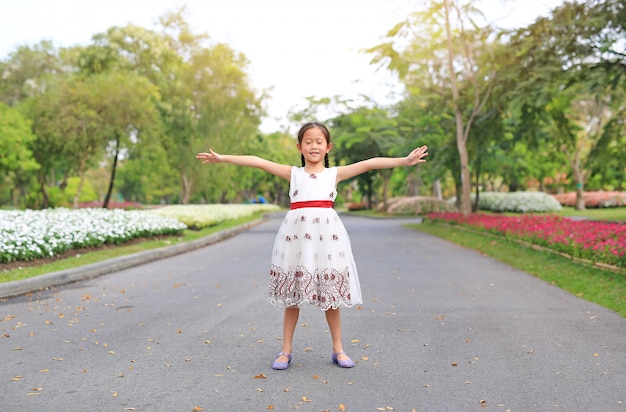 Portrait of happy little girl closed eyes and open wide her arms standing on road in the garden.
