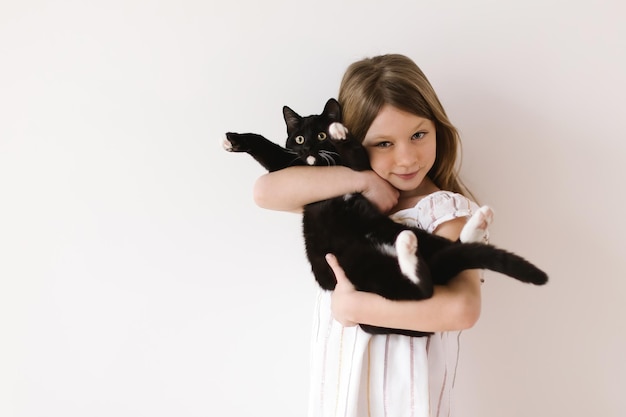 Portrait of happy little girl holding her black cat against a neutral white background