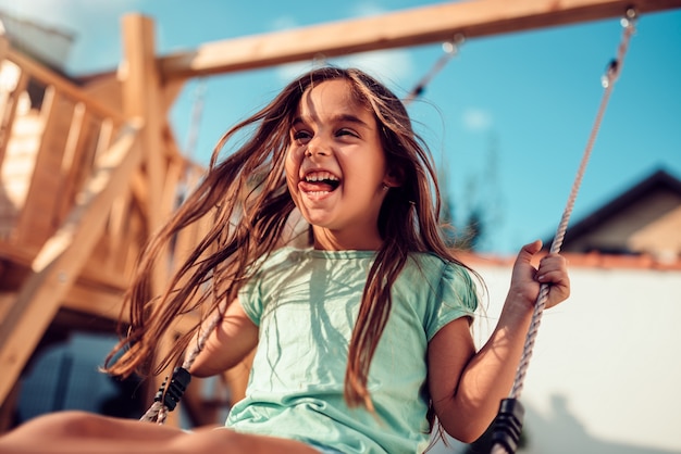 Photo portrait of a happy little girl sitting on a swing and smiling