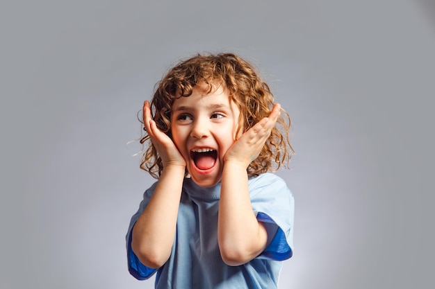 Portrait of a happy little girl with curly hair She stands on a gray background and expresses an emotion of joy