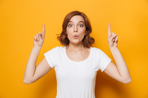 Portrait of a happy lovely girl standing isolated over yellow wall, pointing at copy space