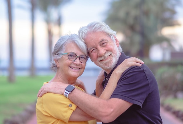 Portrait of happy lovely senior couple embracing in outdoor public park at sunset Two caucasian elderly people looking at camera smiling enjoying good time together