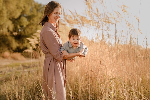 Portrait of happy loving mother hugging her baby son in the sunny park near river