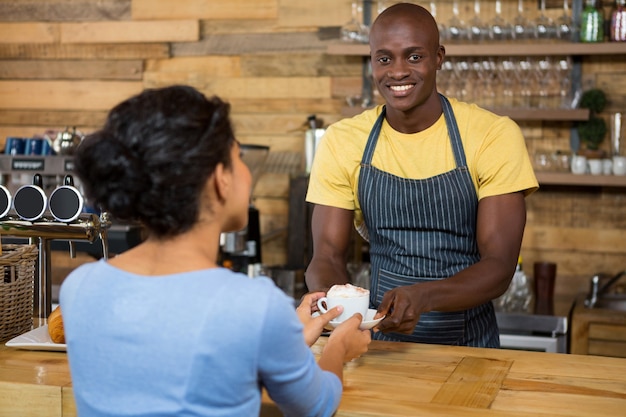 Portrait of happy male barista serving coffee to customer in coffee shop
