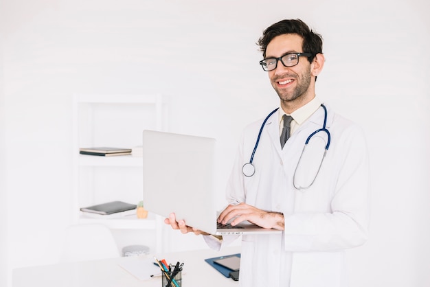 Ritratto di un medico maschio felice che per mezzo del computer portatile