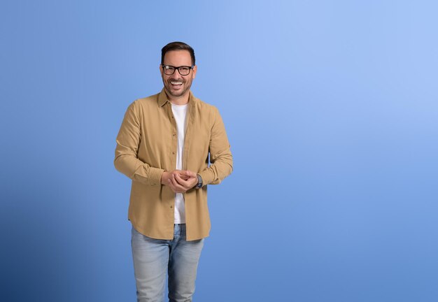 Portrait of happy male professional with hands clasped and in eyeglasses posing on blue background