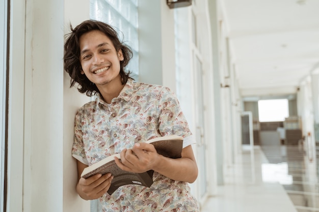 Portrait of happy male student holding book and looking at camera on campus.