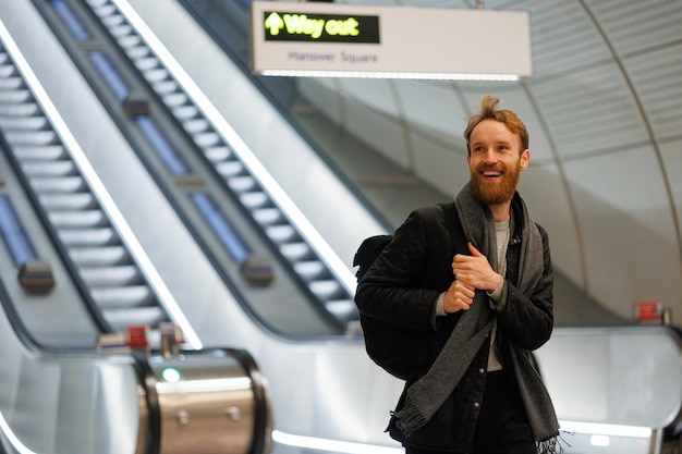 Photo portrait of happy male tourist with backpack on background of escalators at train station or airport