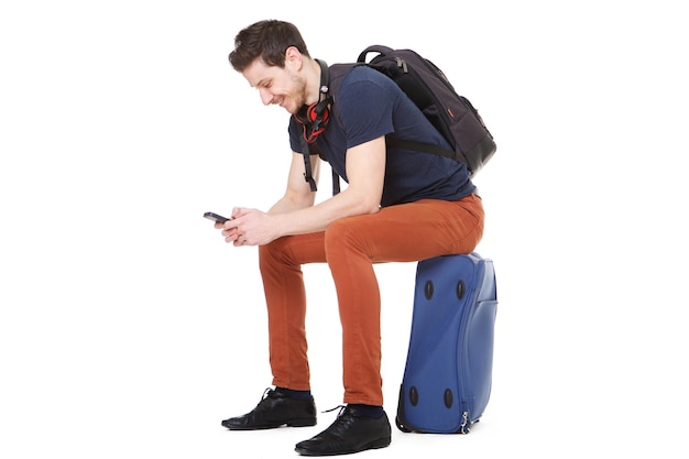 スーツケースの上に座って携帯電話を見ている幸せな男性旅行者の肖像画