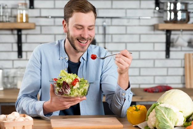 Photo portrait of a happy man eating fresh salad in the kitchen