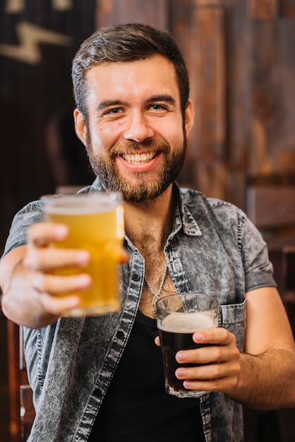 Photo portrait of a happy man holding glasses of rum and beer