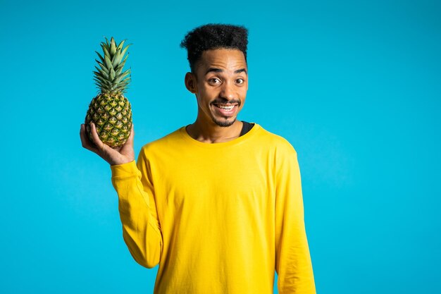 Photo portrait of happy man holding pineapple against blue background