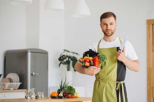 Portrait of a happy man holding a plate of fresh vegetables on the background of the kitchen at home