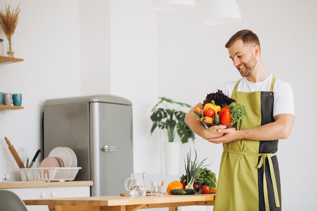 Portrait of a happy man holding a plate of fresh vegetables on the background of the kitchen at home