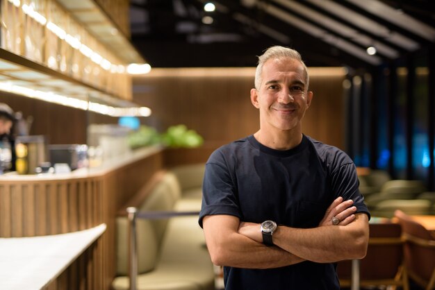 Portrait of happy man inside coffee shop at night smiling with arms crossed, horizontal shot