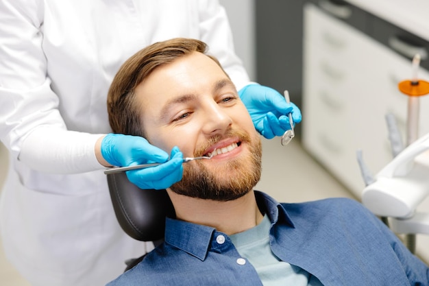 Portrait of happy man sitting at dentist chair in modern clinic and smiling Patient enjoying dental treatment with professional stomatolog