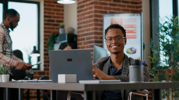 Ritratto di uomo felice che utilizza il laptop per lavorare sulle statistiche aziendali, analizzando i grafici aziendali con i dati per la soluzione di sviluppo. giovane con disabilità al lavoro d'ufficio. colpo a mano libera.
