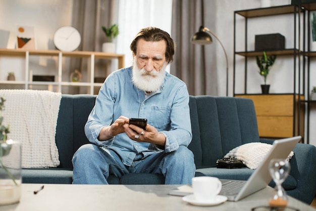 Portrait of happy man with grey beard mature male in casual wear holding smartphone in hands