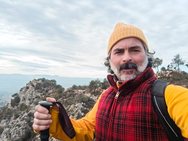 portrait of happy man with walking stick standing on top of mountain