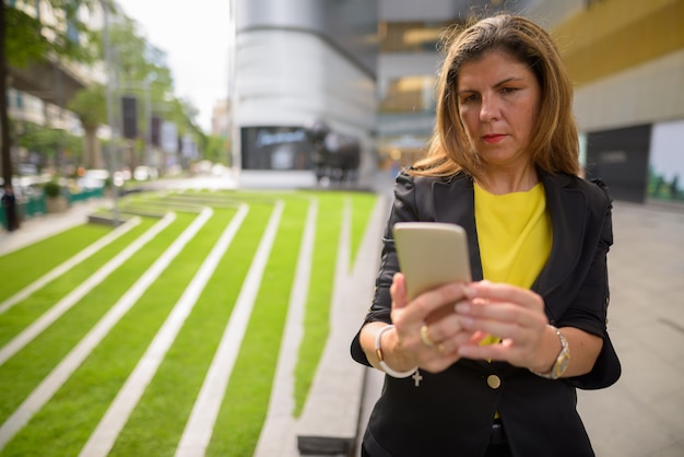 Portrait of happy mature businesswoman using mobile phone outdoors