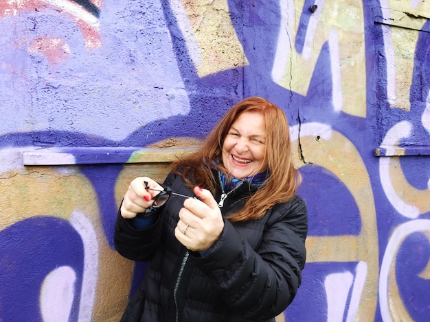 Portrait of happy mature woman standing against graffiti wall